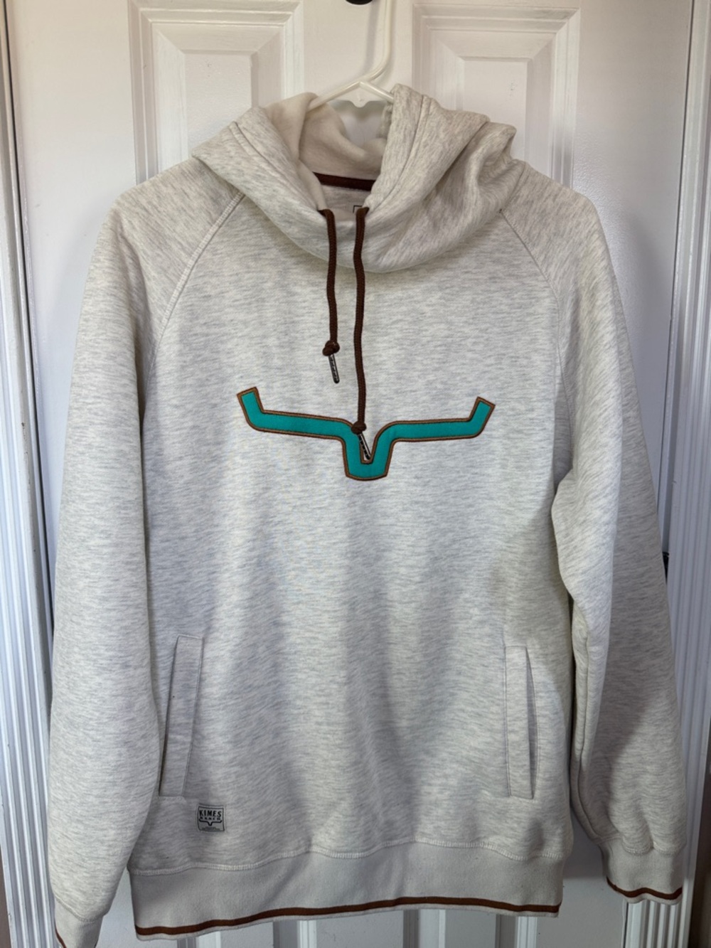 Kimes Ranch Cream Hoodie with Teal Chest Emblem and Brown Accents